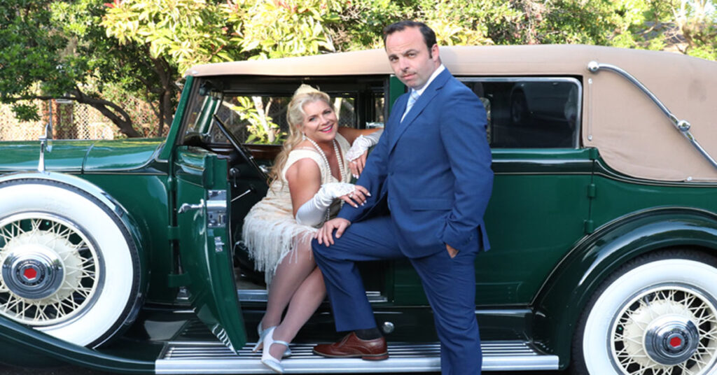 [image: lisa mallette and george psarras posing in front of a 20's style car.]