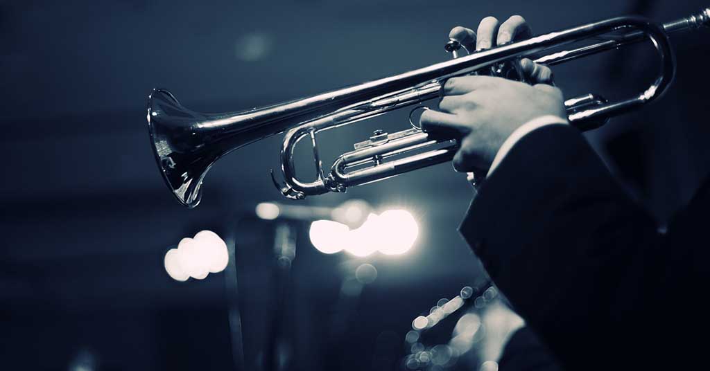 [image: Hands of a person playing a trumpet in a black-and-white image]