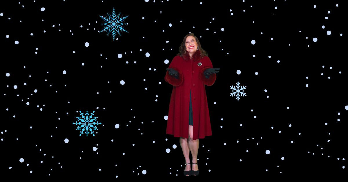 [image: White woman with a long red winter coat and a big smile, turning her palms up to the images of snowflake graphics falling from above]