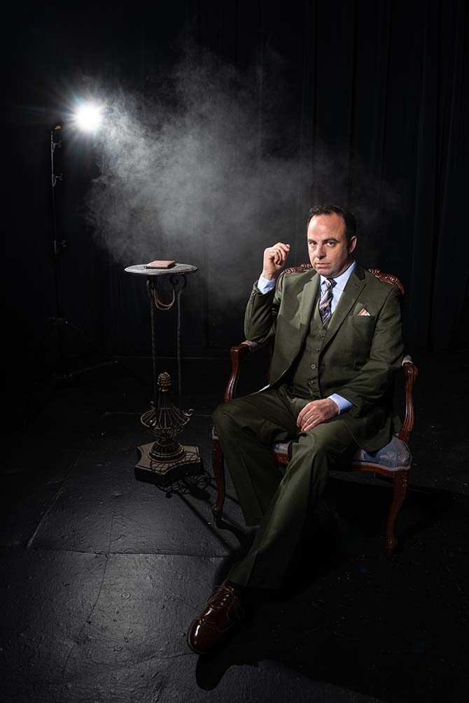 An actor in 1950s film noir garb, viewed under hazy light.