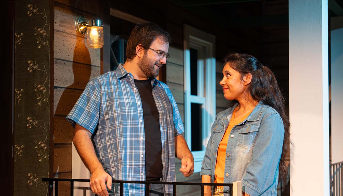 A young man and woman look lovingly at each other while standing on a porch.