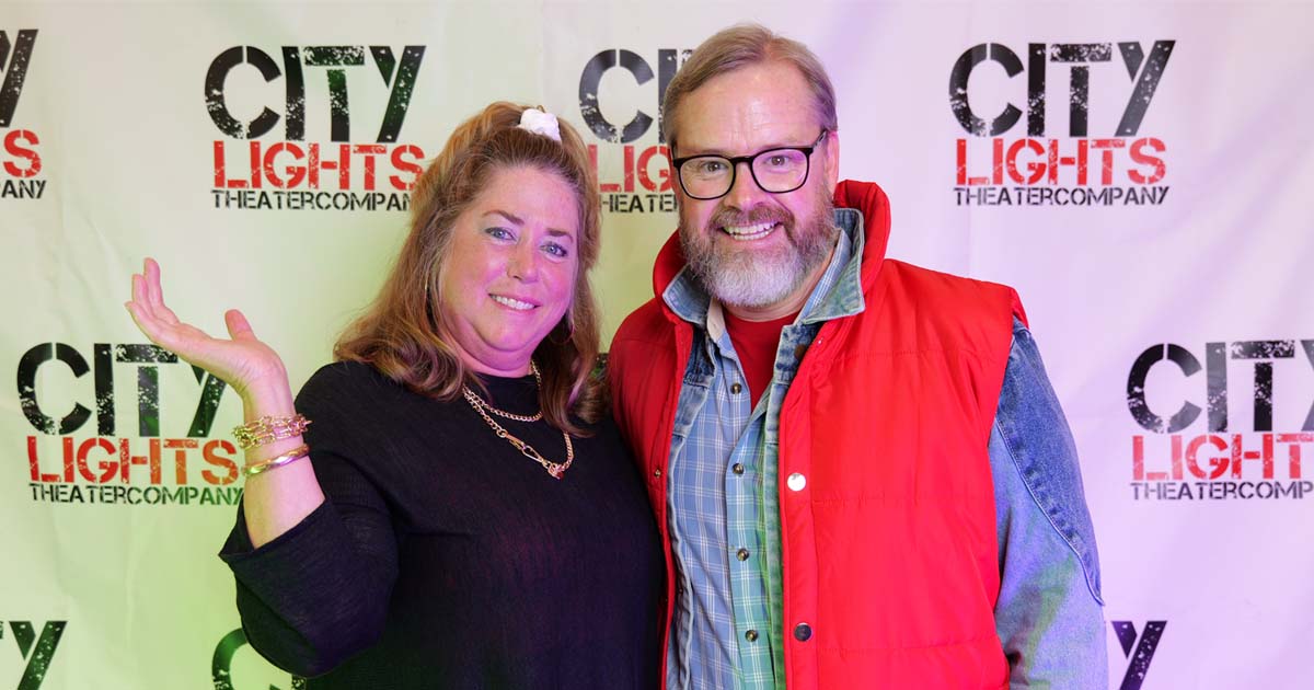 [image: A woman and man in vibrant 1980s dress smiling and posing in front of a wall that says City Lights Theater Company]