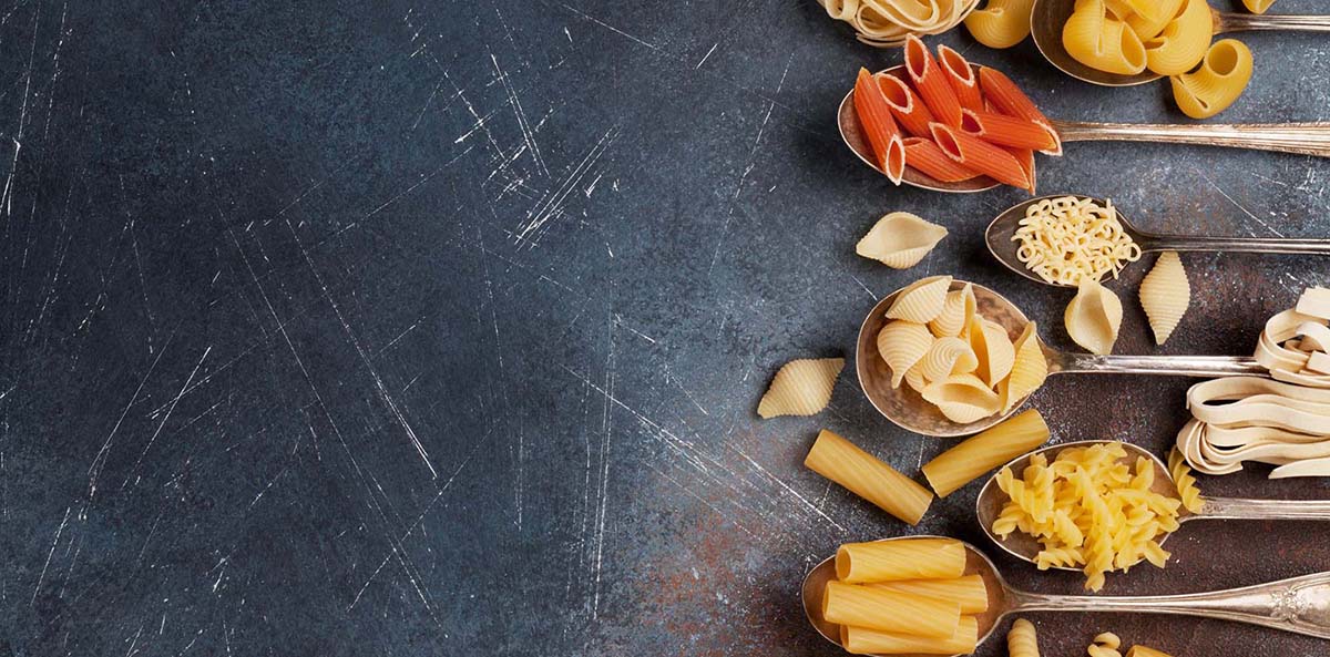 [image: A scatter of various types of dry pasta against a gray background]